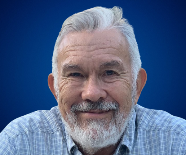 Jimmy Marull, conferencista especializado en deportes y aventuras, sonriendo con una camisa a cuadros y fondo azul.